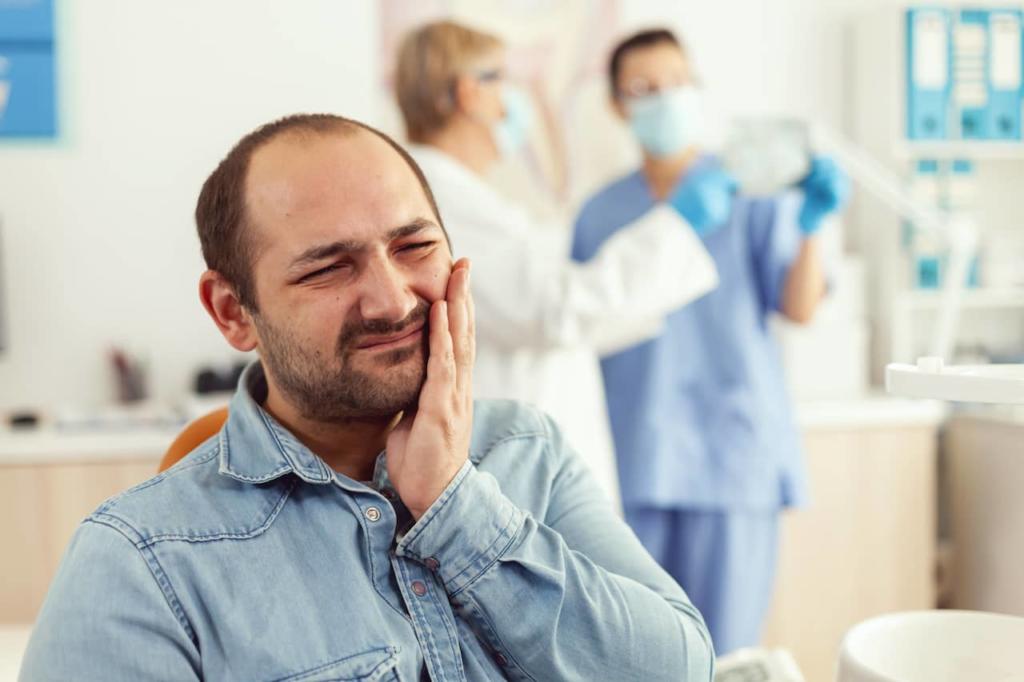 Man showing signs of pain in his mouth with dentists in background.